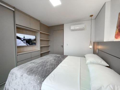 a bedroom with a white bed and a television at Lindo Flat Planejado com Vista Para Cidade in Campo Grande