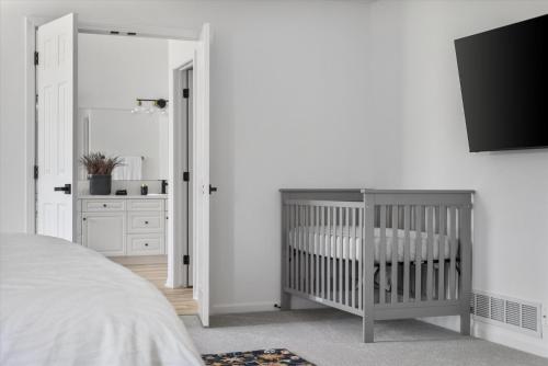 a white bedroom with a crib and a bathroom at 6BR Luxury Stay Prime Spot Games & More in Millard