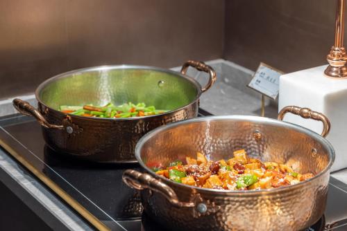 two metal pots sitting on a stove with vegetables at G5 Shang Hotel - Kunming Railway Station Huan Cheng Nan Road Metro Station Branch in Kunming