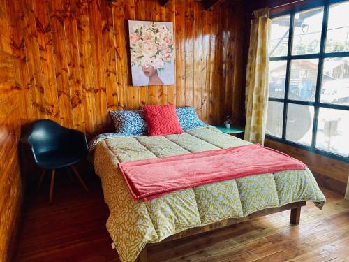 a bedroom with a bed with a red blanket and a chair at Hostal María Lucía in Coñaripe