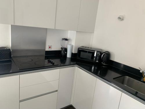 a kitchen with white cabinets and a black counter top at Modern Hi-rse 1bedroom Apartment in Woolwich
