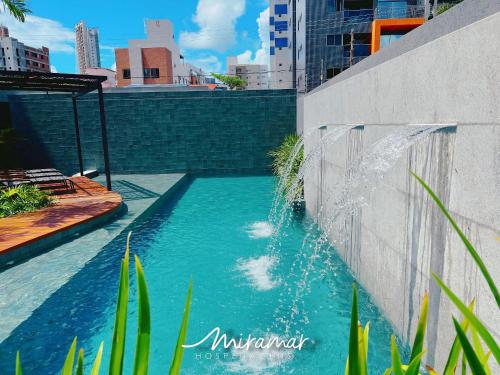 a swimming pool with a fountain in the side of a building at Vert House Jardim Oceania - Miramar Hospedagens in Tambaú