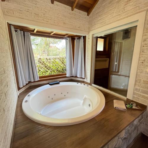 a large white tub in a bathroom with a window at Chale Villa do Valle in Monte Verde