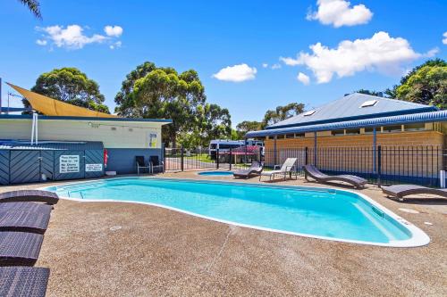 a swimming pool with chairs and a building at Waters Edge Holiday Park in Lakes Entrance