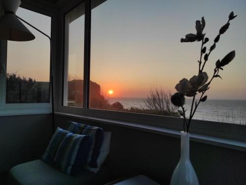 a vase with flowers in a window with a sunset at Holiday home for 8 people in Veulettes-sur-Mer