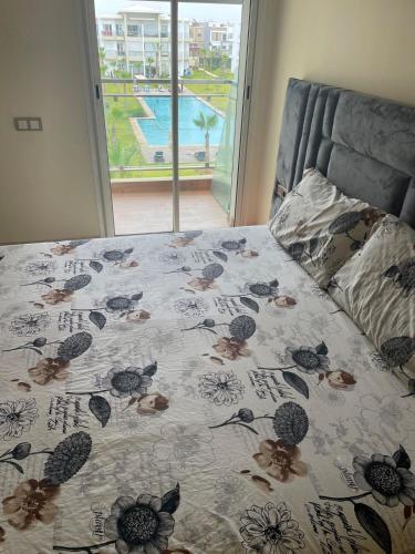 a bed with a flowered bedspread with a view of a pool at À LOUER APPARTEMENT à Casabay in Sidi Rahal