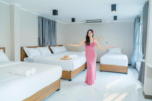 une femme en robe rose debout entre deux lits dans l'établissement บีบีพลูวิลล่า2025, à Nong Prue