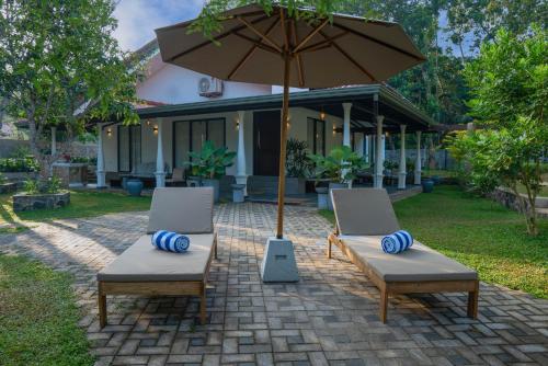 two chairs and an umbrella in front of a house at Samadhi Lagoon Villa in Rathgama