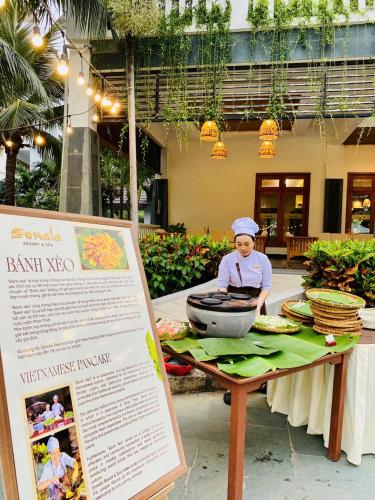 a woman cooking food on a table with a sign at Sonata Resort & Spa in Phan Thiet