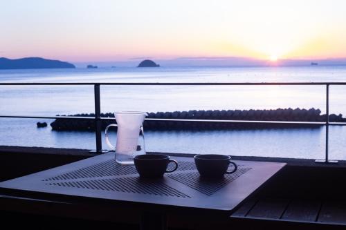 a table with two cups on a balcony with the ocean at Private luxury villa with ocean view Shodoshima in Shodoshima