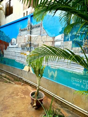 a palm tree in a pot in front of a mural at Mes trois coeurs in Phumĭ Réach Born