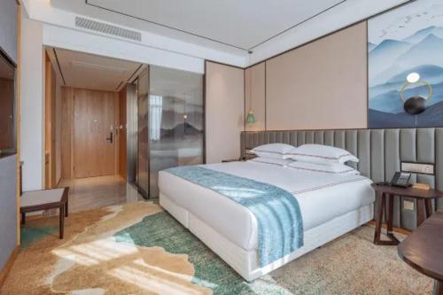 a bedroom with a large white bed and a table at Wellay Hotel Ningbo Jiangbei Olympic Sports Center in Ningbo