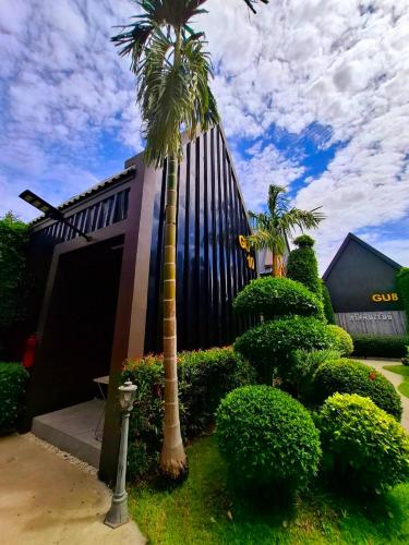 a palm tree in front of a building with bushes at Sawasdee​ Buriram​ Resort in Buriram