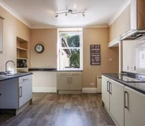 a kitchen with white cabinets and a clock on the wall at Charming Snug Loft Room, Room 4, Beautiful Connel near Oban in Connel