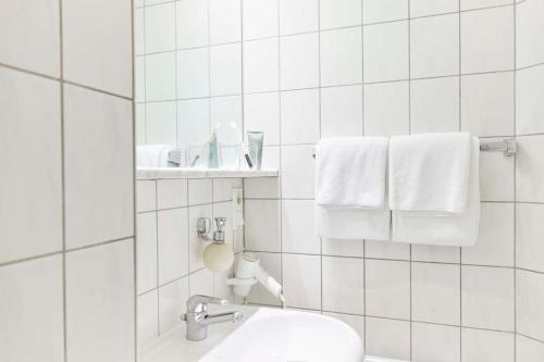 a white tiled bathroom with a toilet and towels at Best Western Raphael Hotel Altona in Hamburg