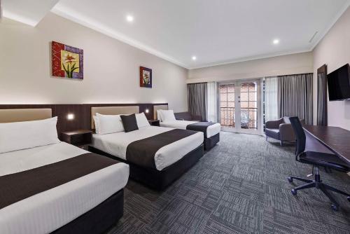 a hotel room with two beds and a desk at Quality Hotel Melbourne Airport in Melbourne