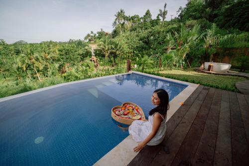 a woman sitting next to a pool with a pizza at CR Tris Casa De Bambú in Selat