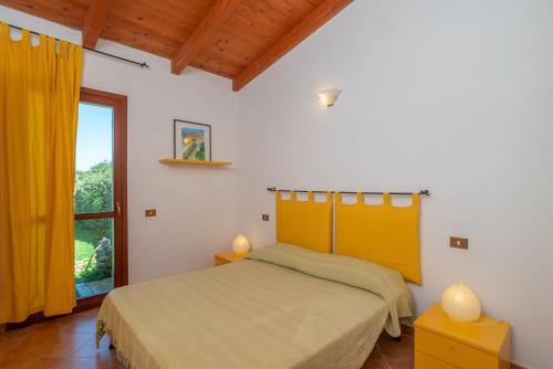 a bedroom with a bed with yellow curtains and a window at Villa Baticle in Santa Teresa Gallura