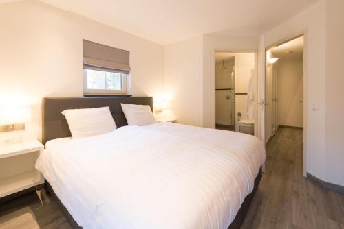 a bedroom with a large white bed with a window at Wilgenhaege Vakantievilla Wellness in Hellendoorn