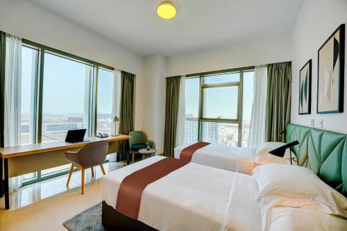 a hotel room with two beds and a desk and windows at Capital Suites Hotel Apartments in Abu Dhabi