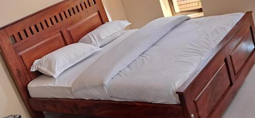 a wooden bed with white sheets and pillows at Urban Nest in Kampala