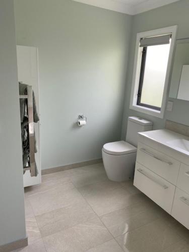 a white bathroom with a toilet and a window at Emerald Haven in Upper Hutt