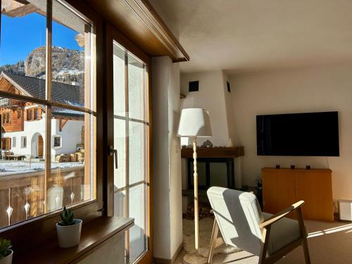 a living room with a window and a chair and a television at Cosy studio apartment in Splügen in Splügen