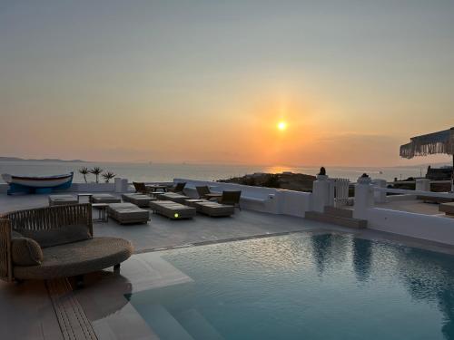 a pool with chairs and a sunset in the background at Paolas Sunset in Agios Stefanos