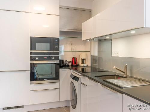 Il comprend une cuisine blanche équipée d'un four micro-ondes et d'un lave-vaisselle. dans l'établissement LARMOR-PLAGE : T2 en résidence de standing avec terrasse et parking, à deux pas de la plage et des commerces - FR-1-349-182, à Larmor-Plage