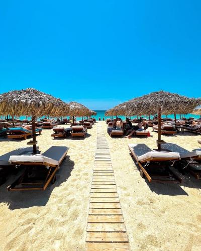 a row of straw umbrellas and chairs on a beach at Apartments Enosis, Alia in Agios Prokopios