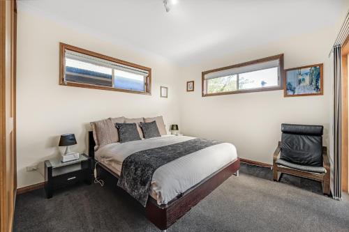 a bedroom with a bed and a chair and two windows at Apartments on Tolmie in Mount Gambier