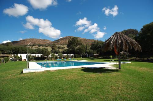a swimming pool with a straw umbrella in a field at TAIGA Tarifa Valdevaqueros in Tarifa
