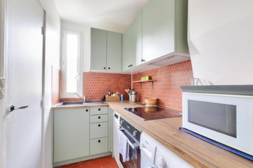 La cuisine est équipée de placards blancs et d'un four micro-ondes blanc. dans l'établissement Cosy 2 BR Flat near Place d'Italie, à Paris