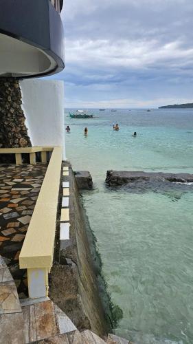 a bench sitting next to the ocean with people in the water at Lydias House kaputian samal in Kaputian
