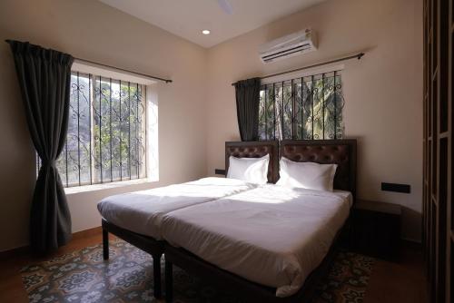 a bedroom with a bed with white sheets and two windows at Hotel Lotus in Candolim