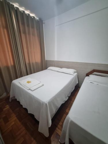 two beds in a room with white sheets at Comodidade e Segurança no Centro in Belo Horizonte