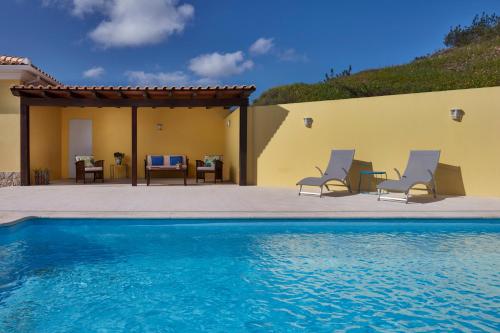 a swimming pool with two chairs and a house at Monte do Forno in Vila Nova De Cacela
