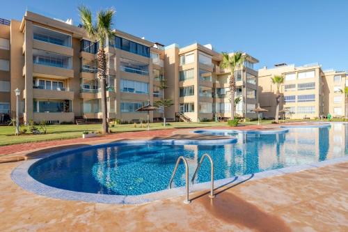 ein Swimmingpool vor einem Gebäude mit Palmen in der Unterkunft Appartement de Luxe - Piscine et Accès à la Plage in Bouznika