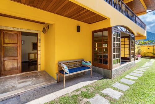 a yellow house with a bench on the porch at Casa Granja Comary - Teresópolis in Teresópolis