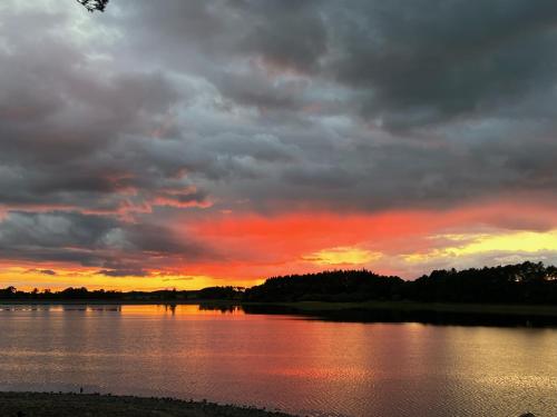 a sunset over a body of water with clouds at Autumn Special Offer - Secluded Luxury Cabins with stream, stargazing, walks and nature - Fell Farm Hideaway in Colwell