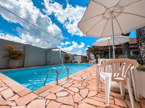 a swimming pool with an umbrella and a chair and a table and an umbrella at Pousada Quinta dos Colibris in São Bento do Sapucaí