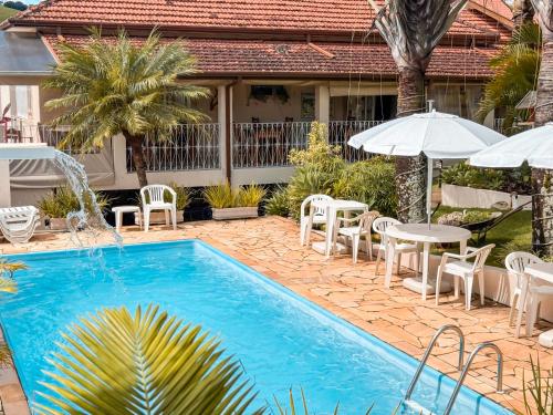 a swimming pool with chairs and tables and umbrellas at Pousada Quinta dos Colibris in São Bento do Sapucaí
