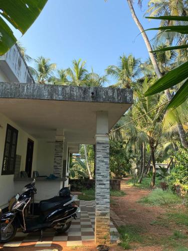 a motorcycle parked outside of a house with palm trees at Thiruthi Homestay in Vallikunnu