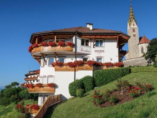 a white building with balconies on a hill with a church at Apartment Residence Egger - n-301 by Interhome in Villandro