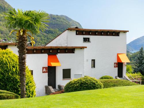 a white building with a palm tree in front of it at Apartment Villaggio Sureggio C10A mit TicinoTicket by Interhome in Lugaggia