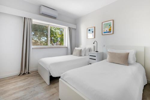 two beds in a white room with a window at Vilar do Golf in Quinta do Lago