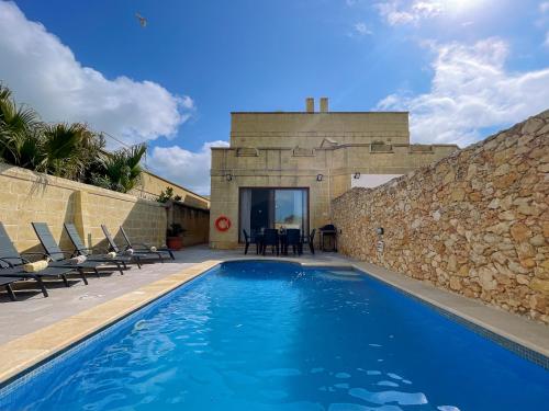 a swimming pool next to a building with a stone wall at Villa Fieldview - Gozo Holiday Home in Għarb