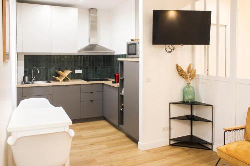 Il comprend une cuisine avec des placards blancs et une télévision murale. dans l'établissement Charming apartment in the heart of the 18th, à Paris