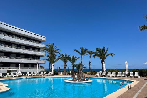 a swimming pool with palm trees and chairs and a building at Palmera Beach by Renthas in Pilar de la Horadada