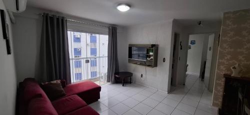 a living room with a red couch and a tv at Apto espaçoso uma quadra do mar com garagem in Balneário Camboriú